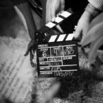 Black and white photo of hands holding a clapperboard on a film set, capturing cinematic action.